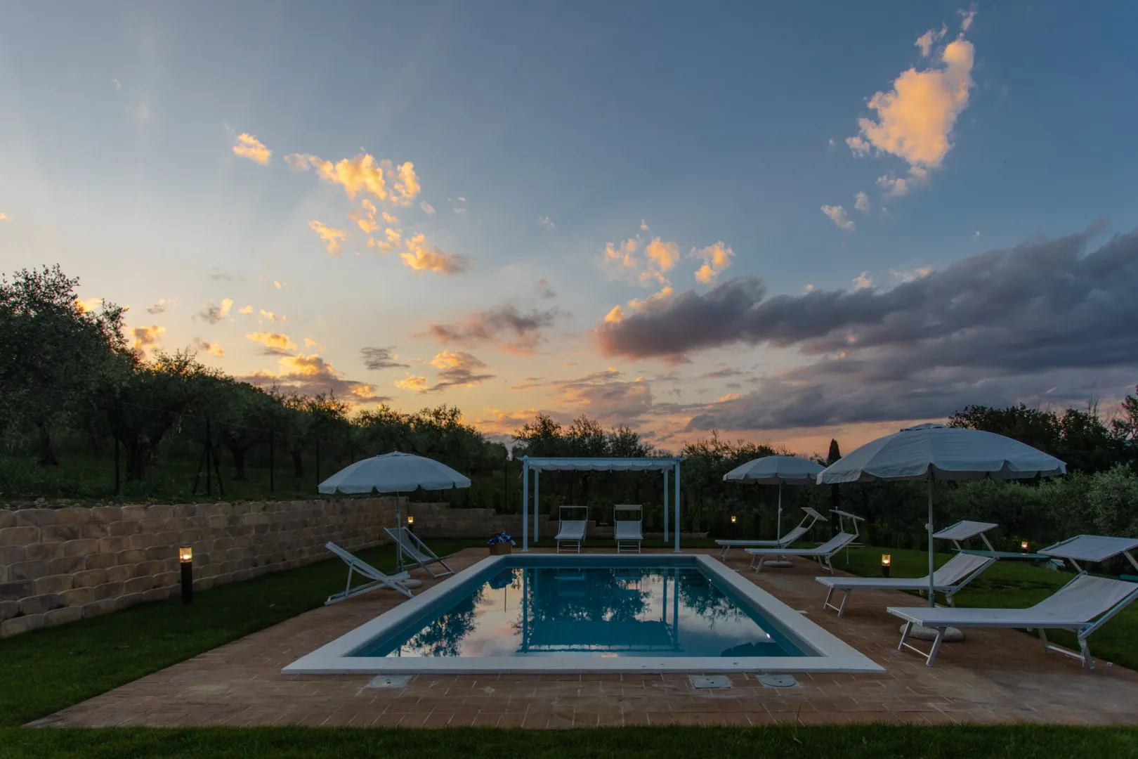An outdoor swimming pool with lounge seating beneath a colorful evening sky.