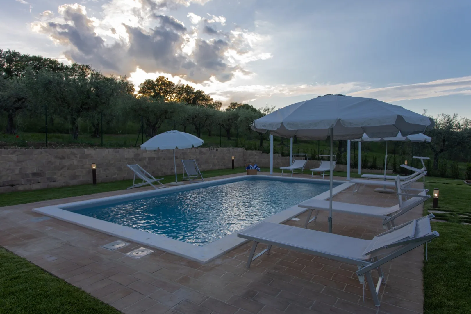 An outdoor swimming pool with lounge seating and umbrellas at sunset.
