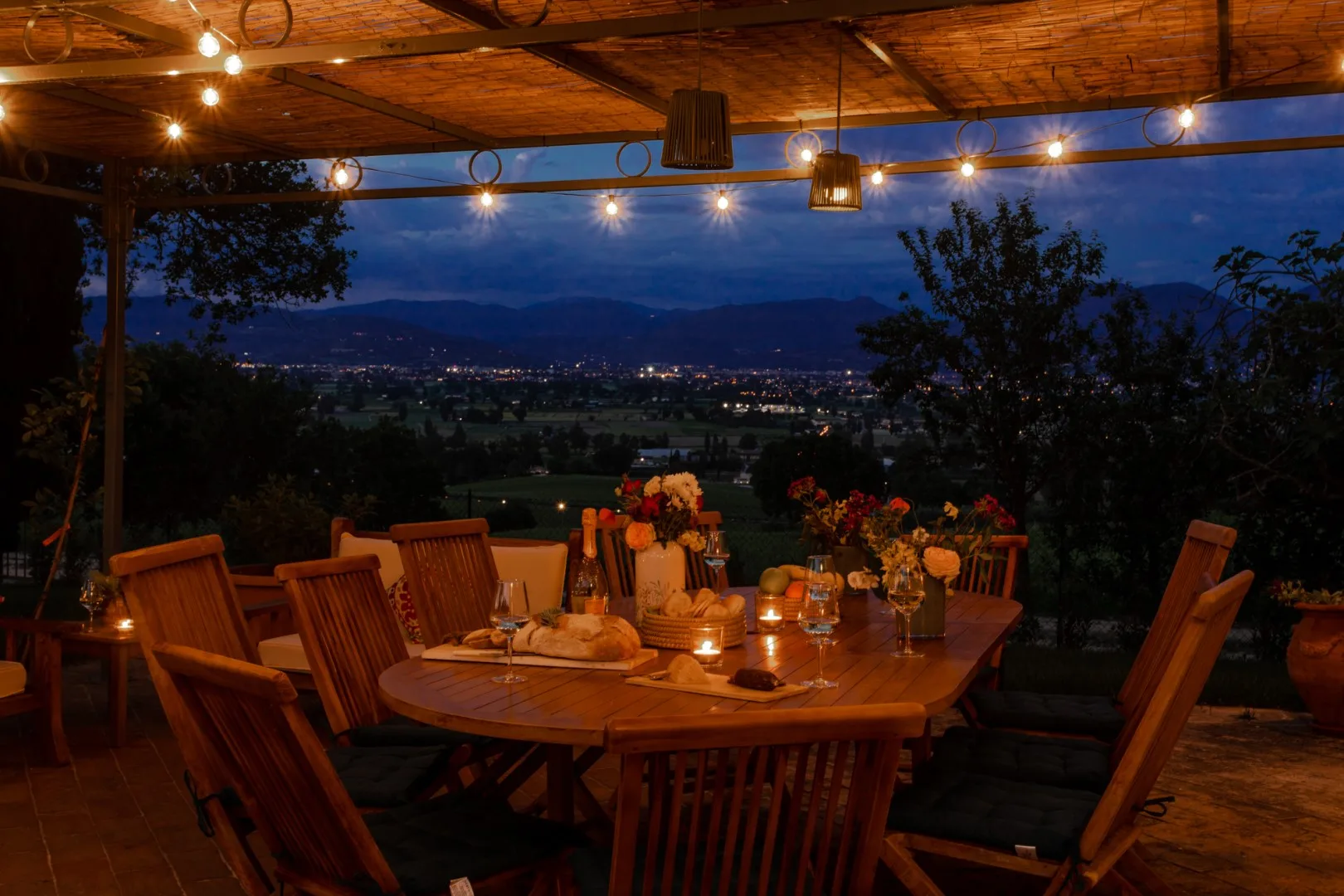 A warmly lit outdoor dining area overlooks a valley at dusk.