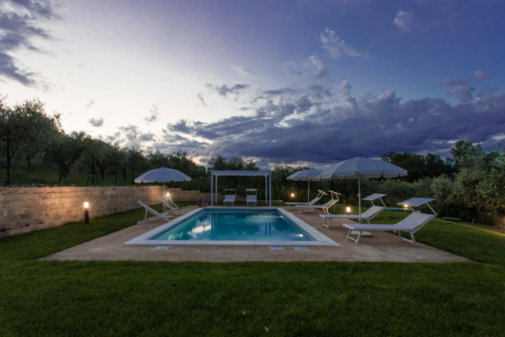 An outdoor pool area with lounge seating beneath a cloudy evening sky.