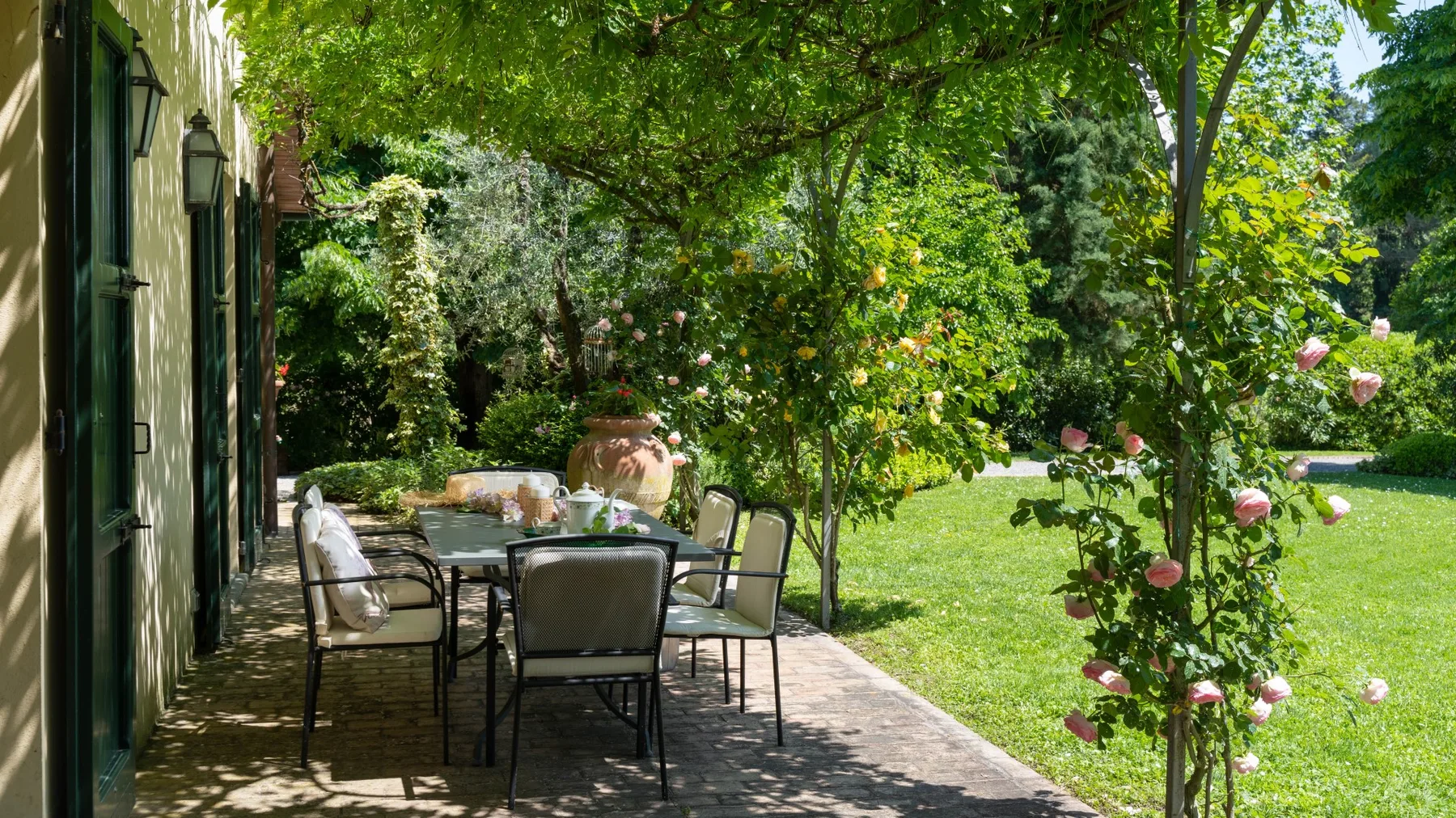 Un patio de jardín sombreado con asientos al aire libre junto a un césped verde.