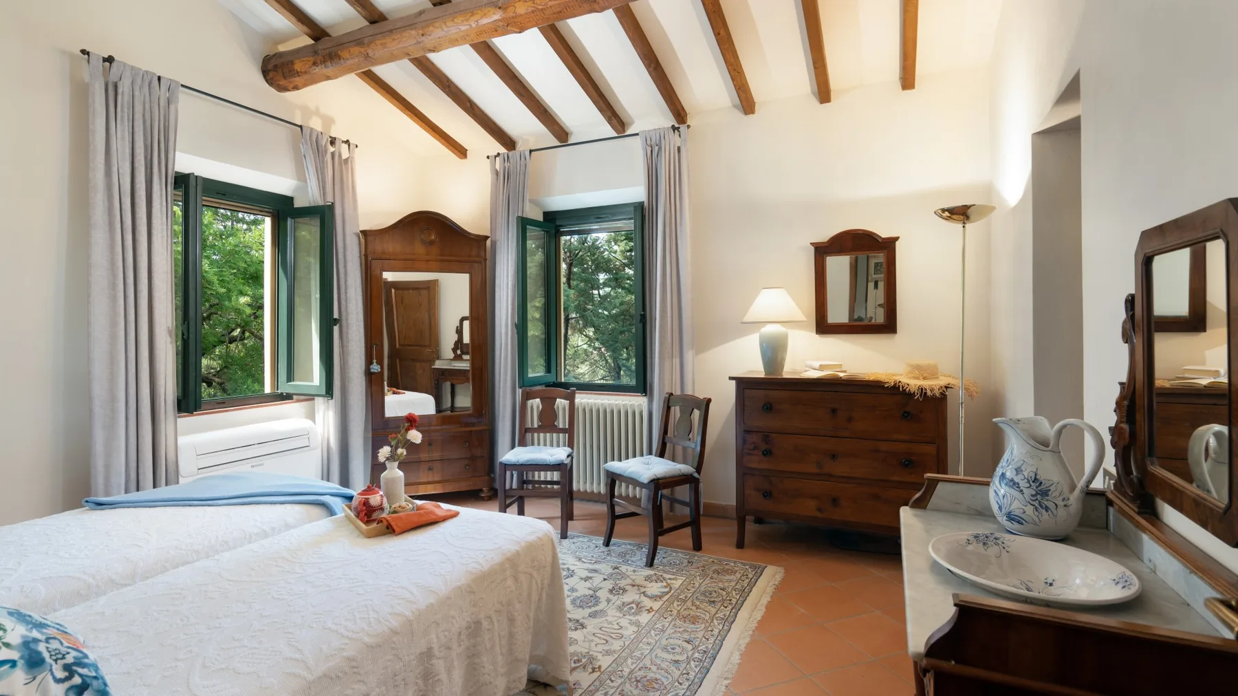 Un dormitorio luminoso con cama, muebles de madera y ventanas con vistas a la vegetación.