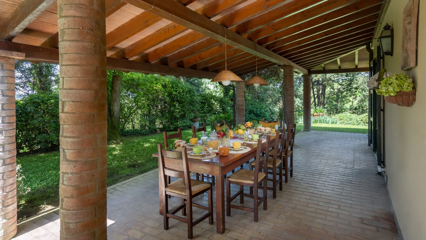 Un comedor exterior cubierto con una mesa larga de madera y vegetación de jardín.