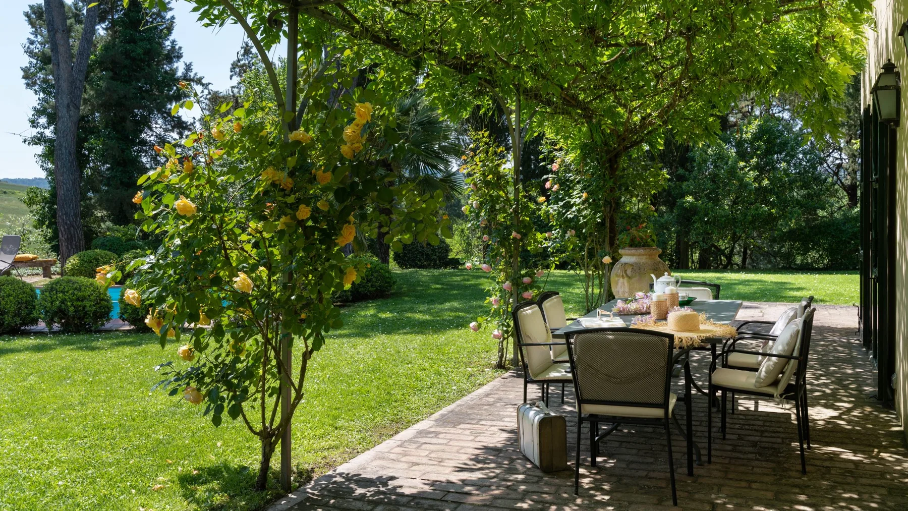 Un patio ajardinado con asientos al aire libre bajo la sombra de los árboles.