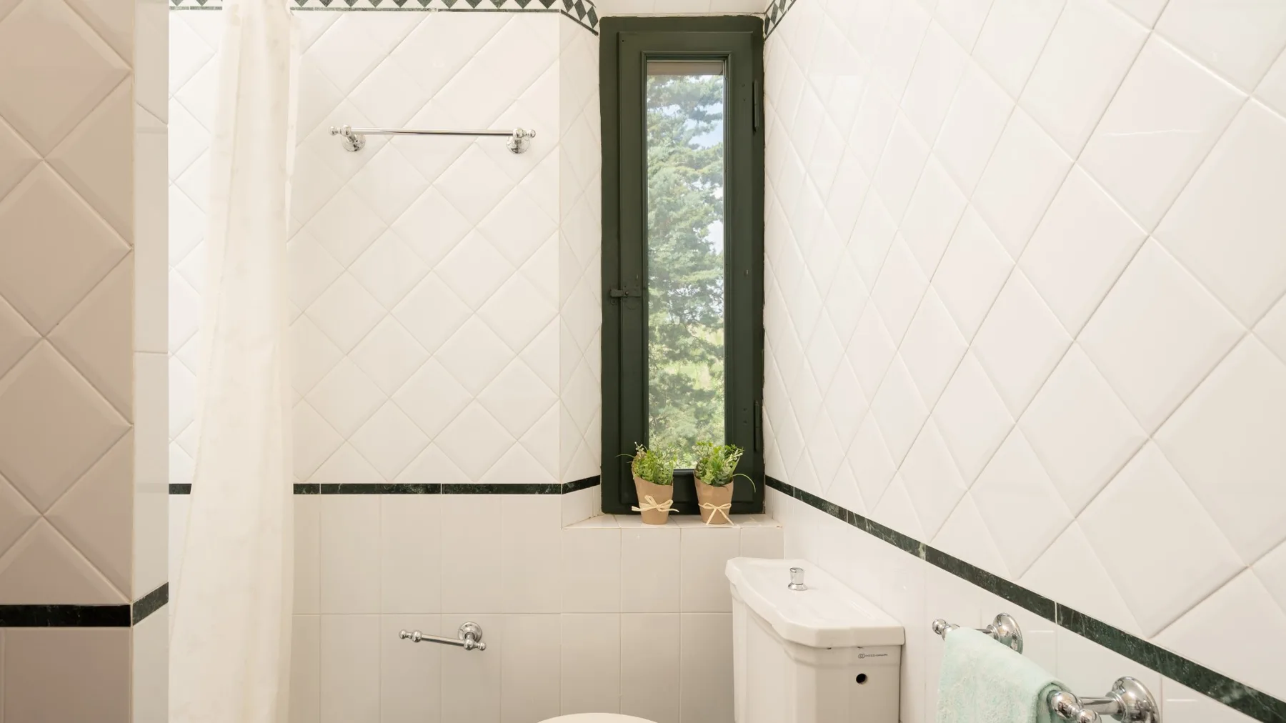Un baño revestido de azulejos con una ventana estrecha y grifería de ducha en la pared.