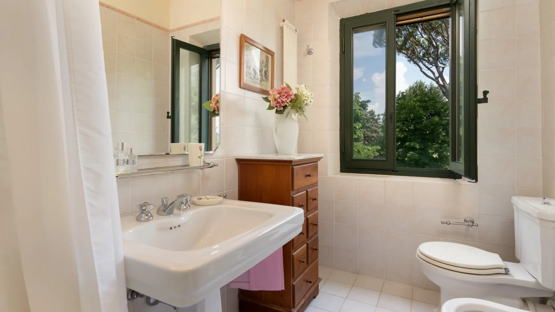 Un baño con azulejos, lavabo, inodoro y una ventana con vistas a la vegetación.