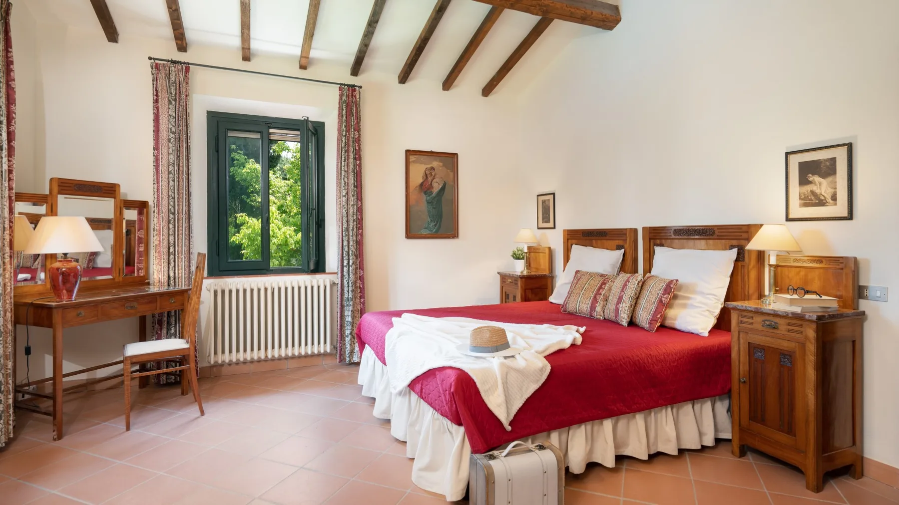 Un dormitorio con una colcha roja, mesitas de madera y una ventana.