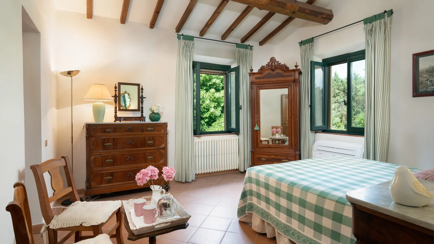 Un dormitorio con una colcha a cuadros, muebles de madera y ventanas con vistas a la vegetación.
