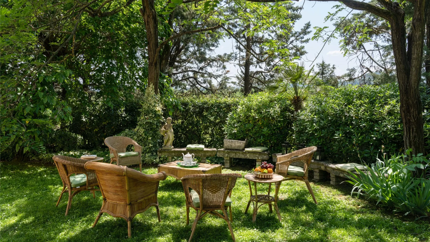 Una zona de estar en el jardín con sillas de mimbre y una mesa bajo árboles frondosos.