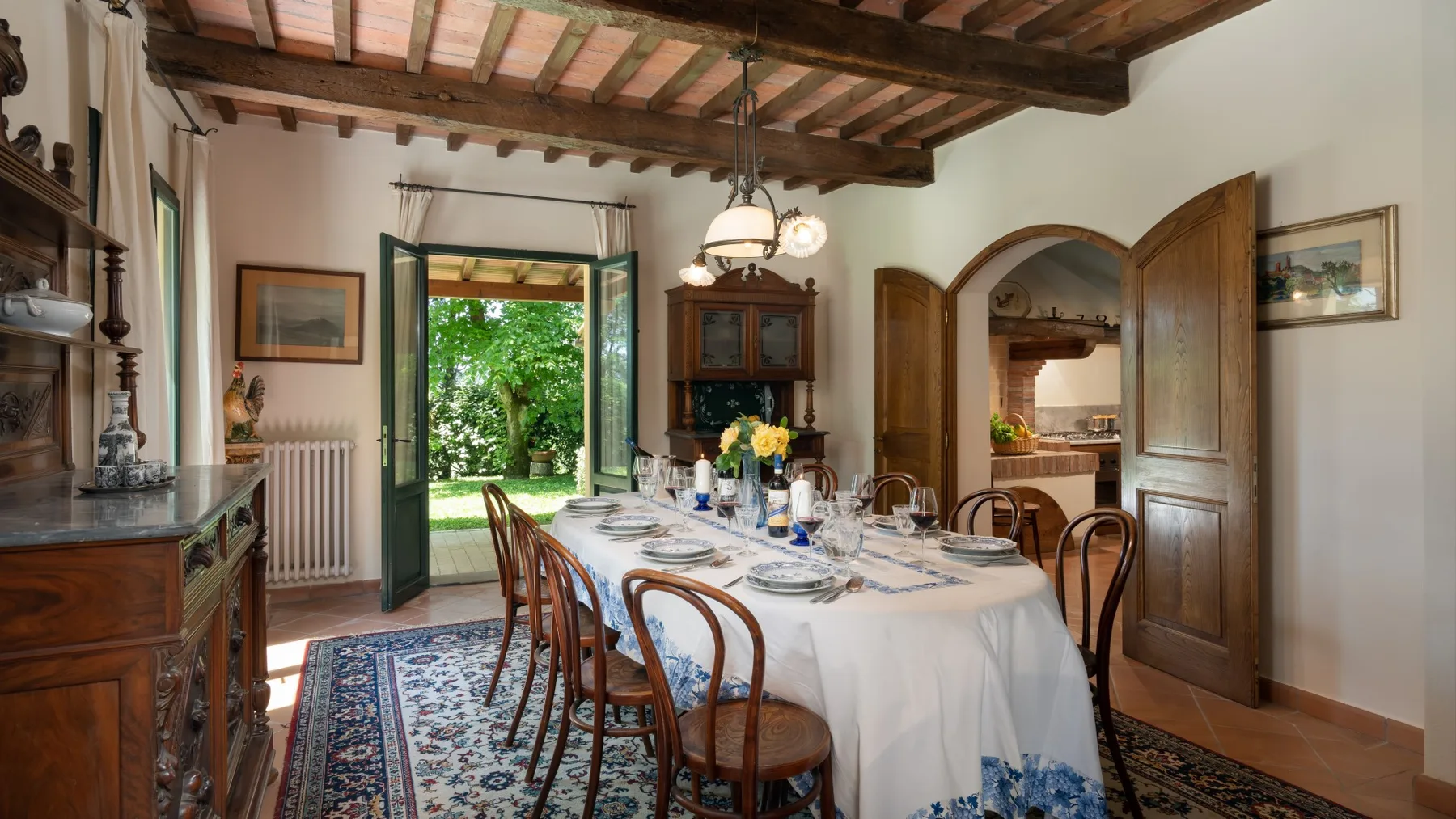 Un comedor con una mesa larga junto a puertas abiertas al jardín.