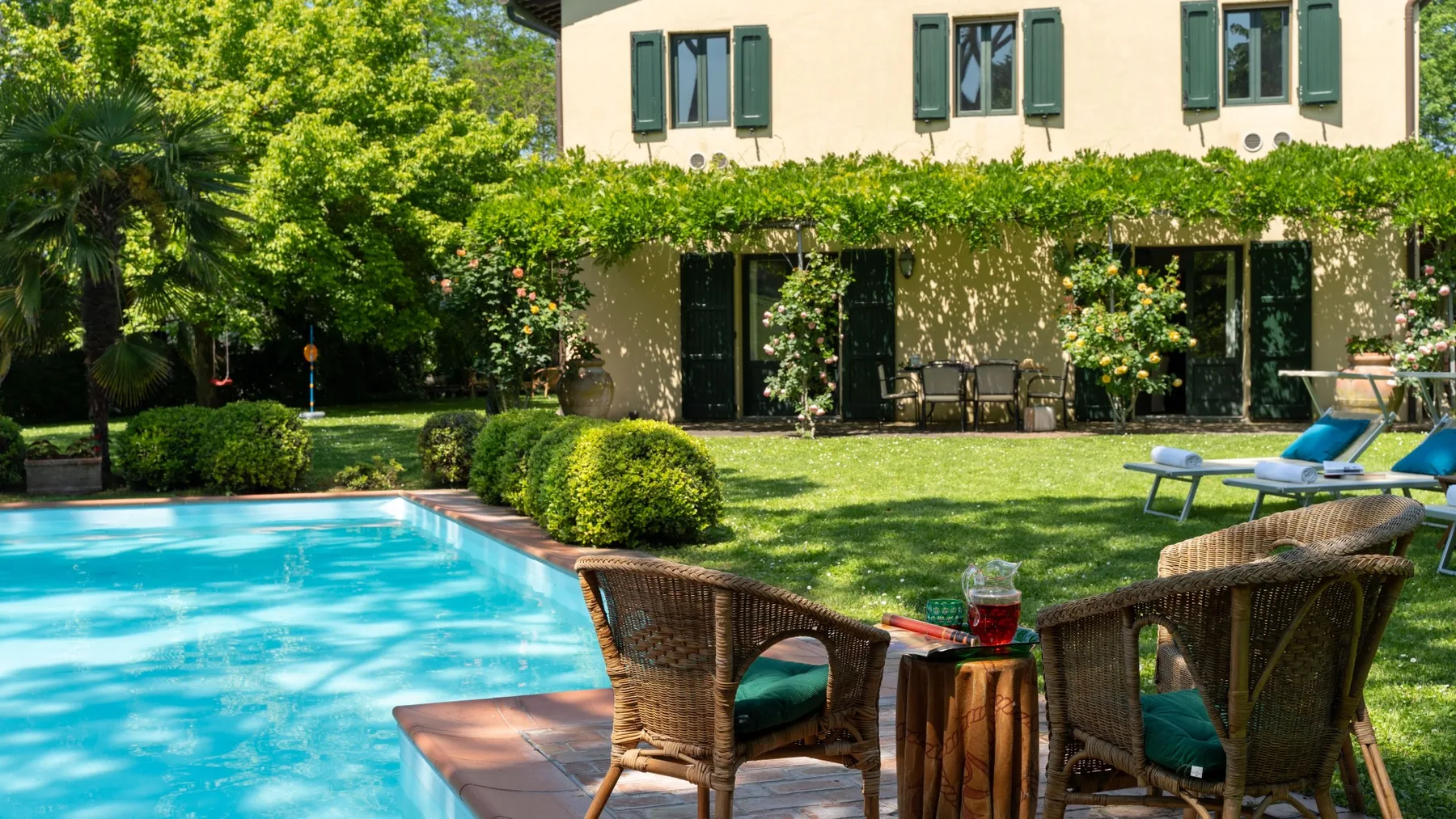 Un patio ajardinado junto a una piscina, con asientos al aire libre y vegetación.