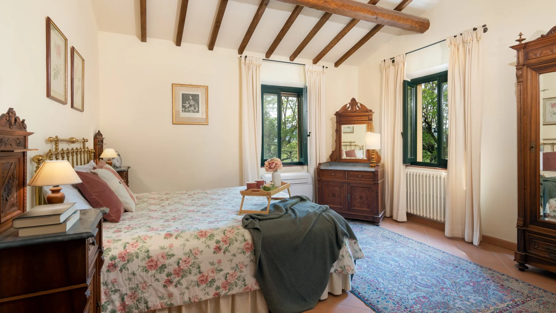 Un dormitorio con ropa de cama floral, muebles de madera oscura y ventanas con cortinas.
