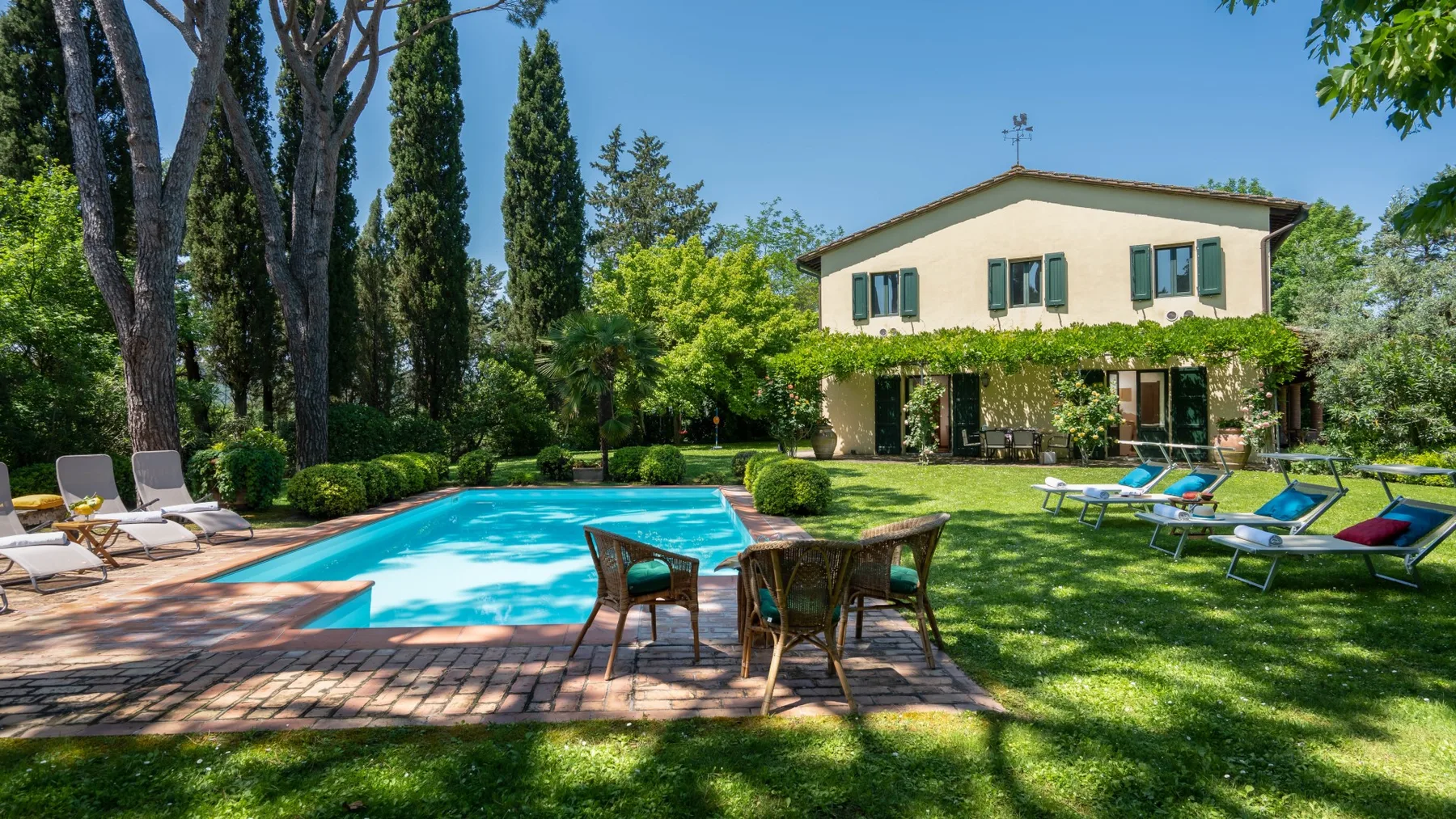 Un jardín con piscina, asientos al aire libre y una casa al fondo.
