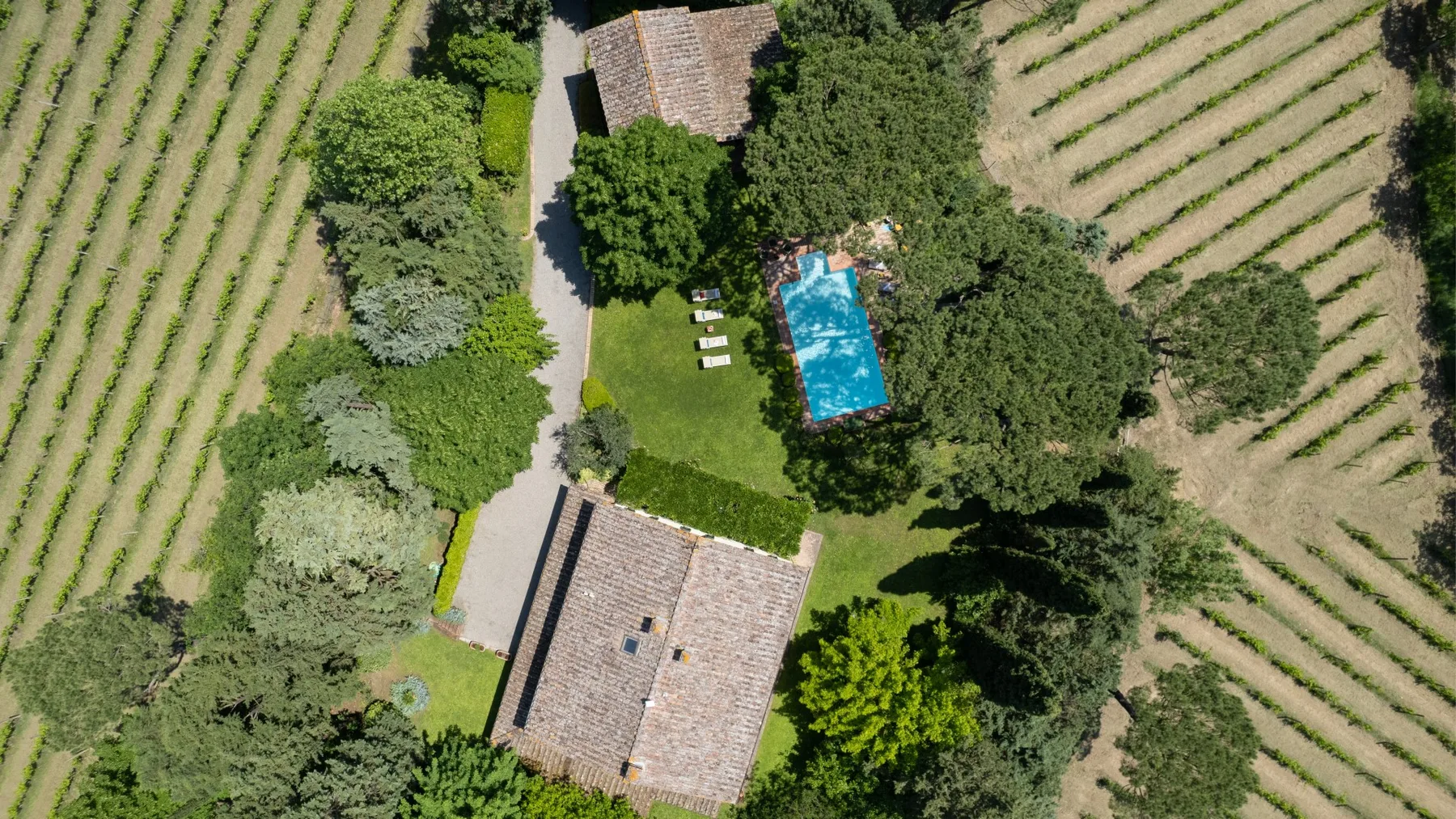 Vista aérea de una propiedad rural con piscina entre árboles y campos cultivados.