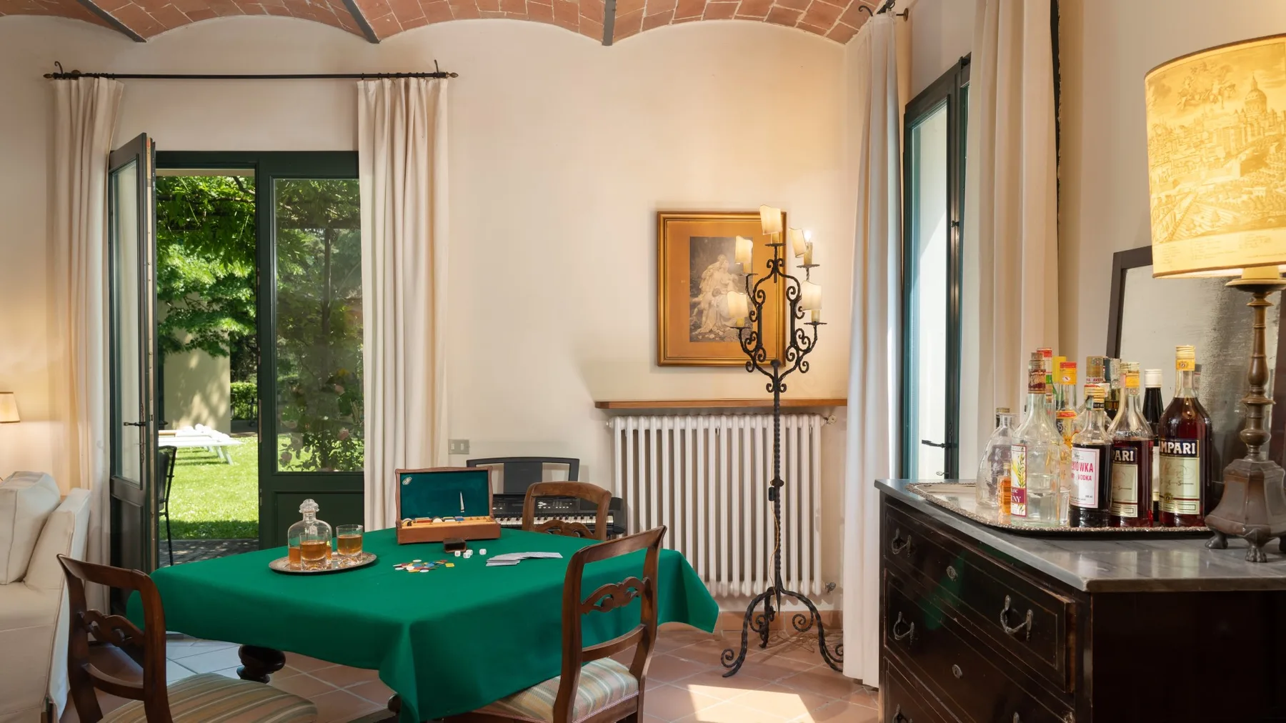 Un comedor con una mesa cubierta de verde junto a ventanas altas que dan a un jardín.