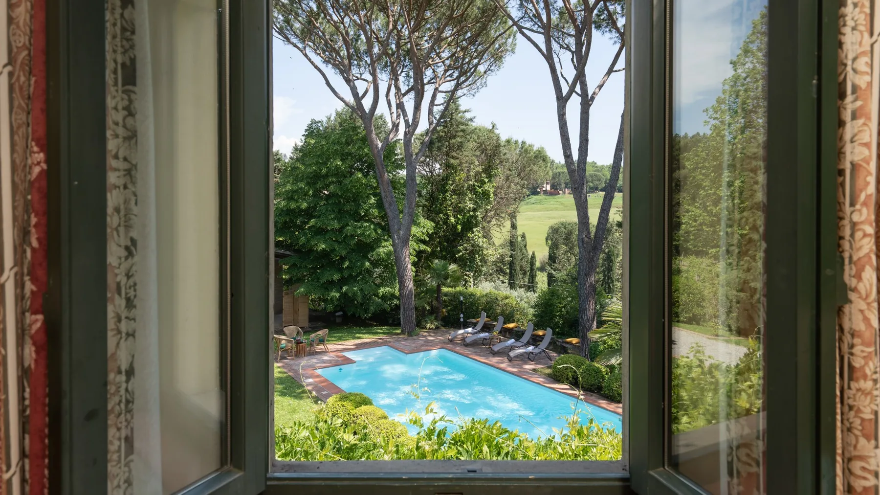 Se ven una piscina y un jardín a través de una ventana abierta.