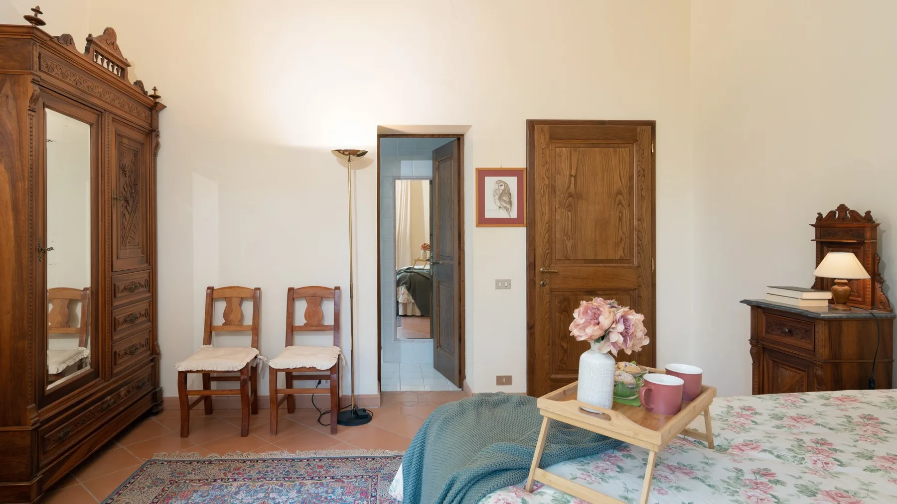 Un dormitorio con una cama, un armario de madera, sillas y una mesita.