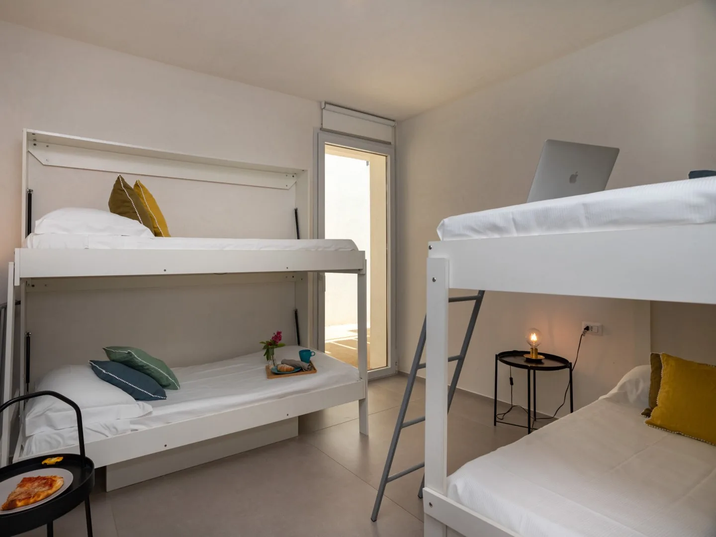 Un dormitorio luminoso con literas blancas y una mesita junto a la cama.