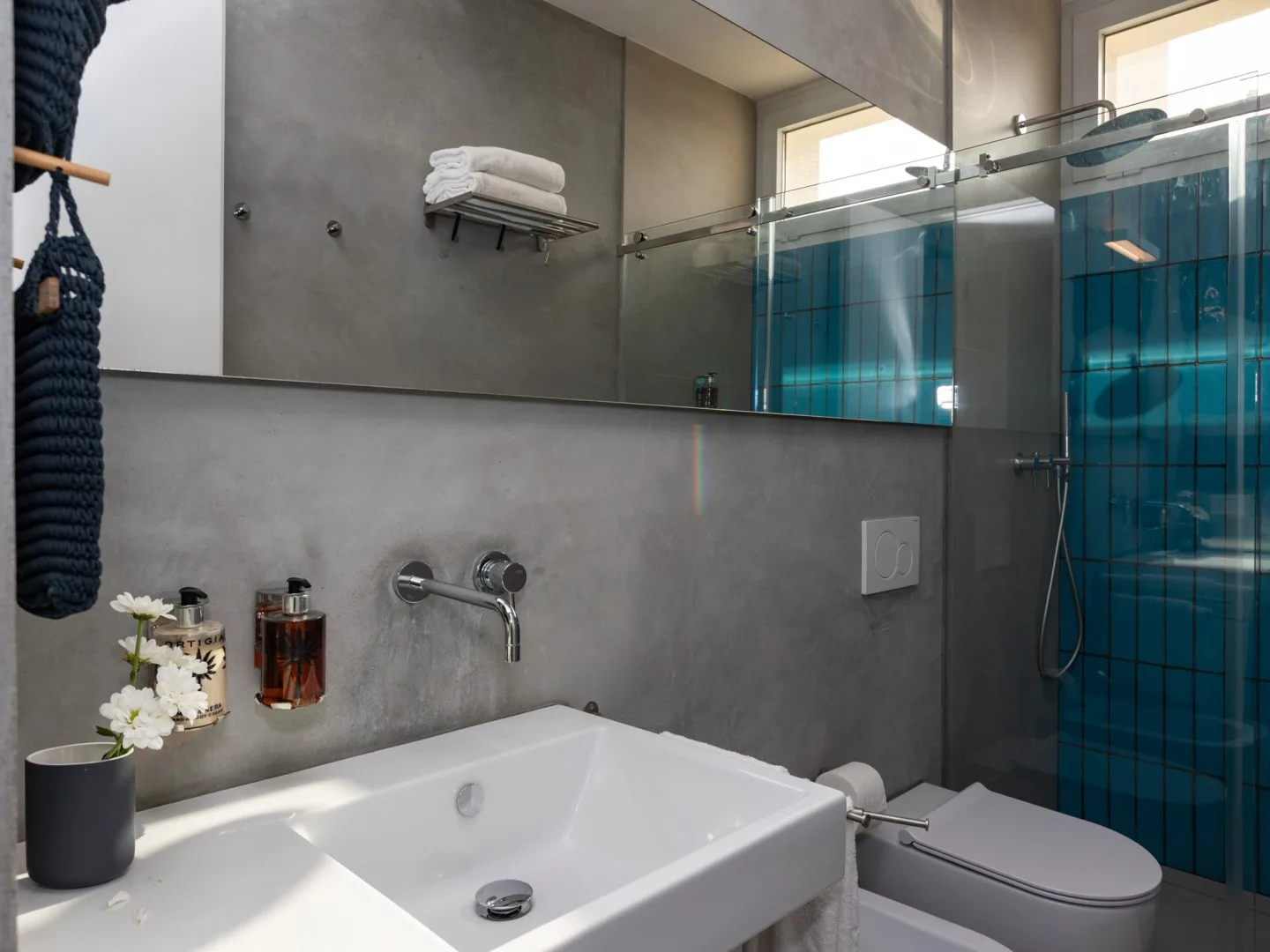 Un baño moderno con un lavabo blanco y una ducha con vidrio azulado.