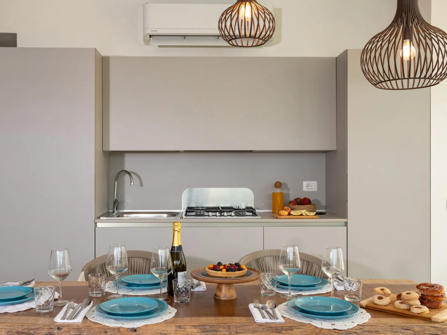 Una mesa está puesta frente a una cocina compacta con placa de cocción y fregadero.