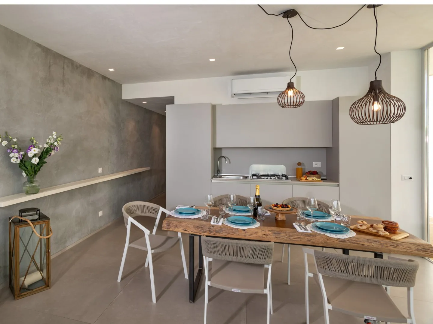 Un comedor con una mesa de madera puesta con platos y luces colgantes.
