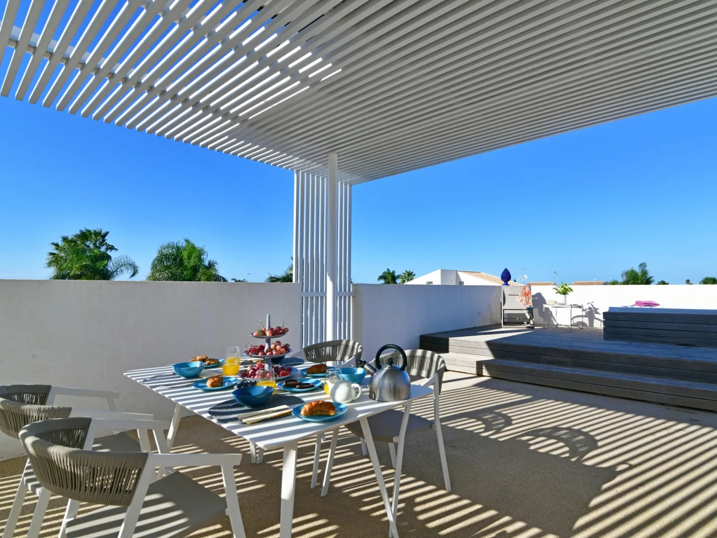 Comedor en la azotea con una mesa puesta bajo una pérgola de listones.