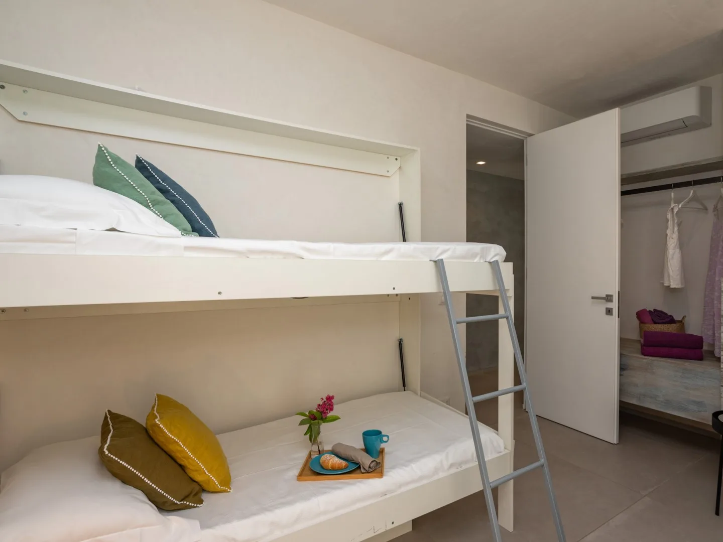 Un dormitorio con una litera blanca, cojines de colores y un armario abierto.