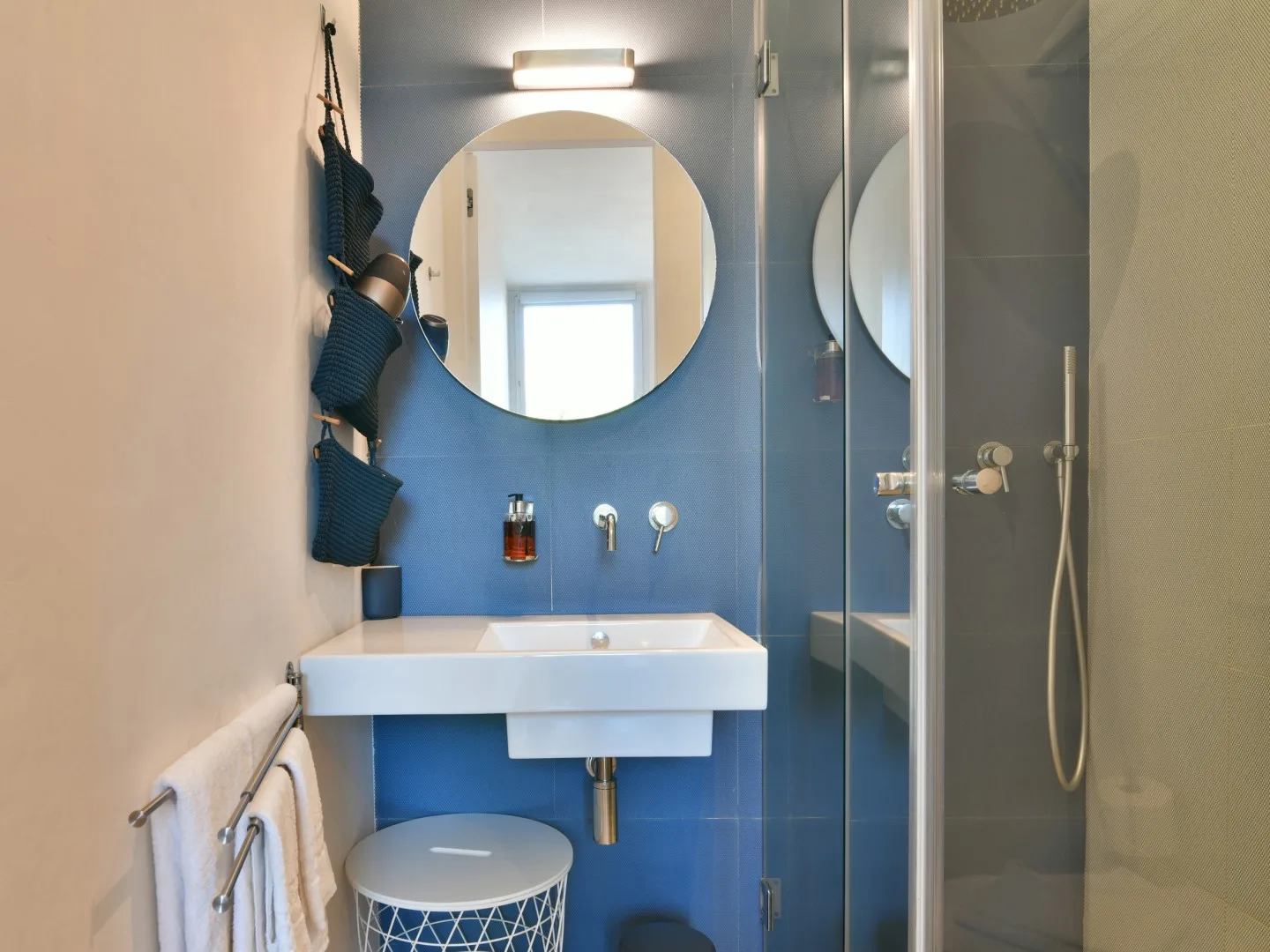 Un baño compacto con lavabo, espejo redondo y ducha de cristal.