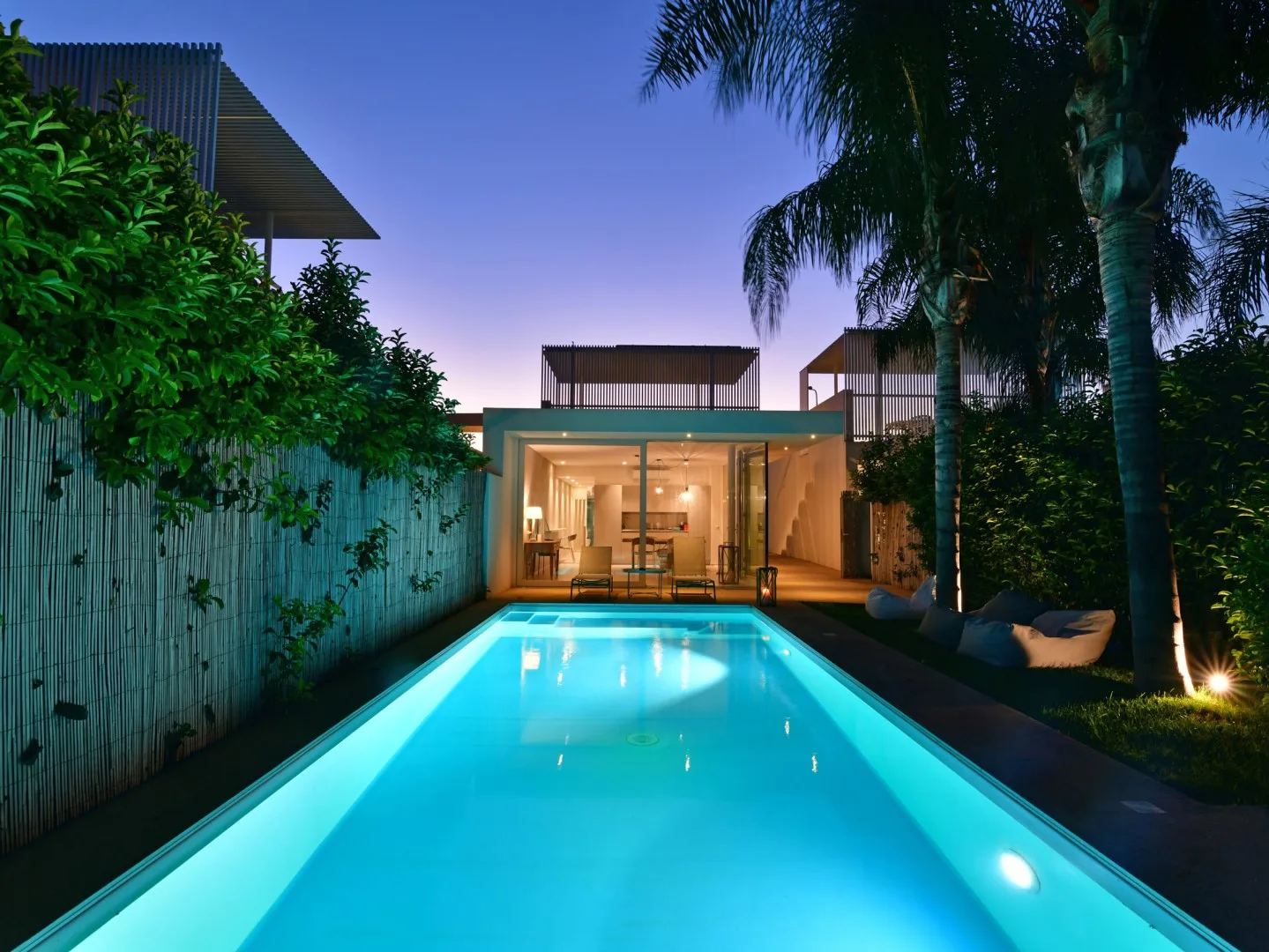 Una piscina iluminada conduce hacia un edificio con fachada de vidrio al anochecer.
