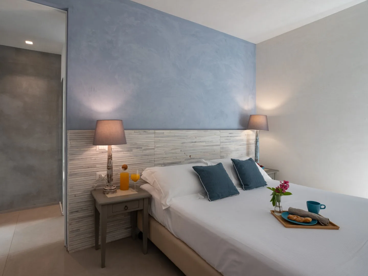 Un dormitorio con una cama bien tendida y lámparas de noche.