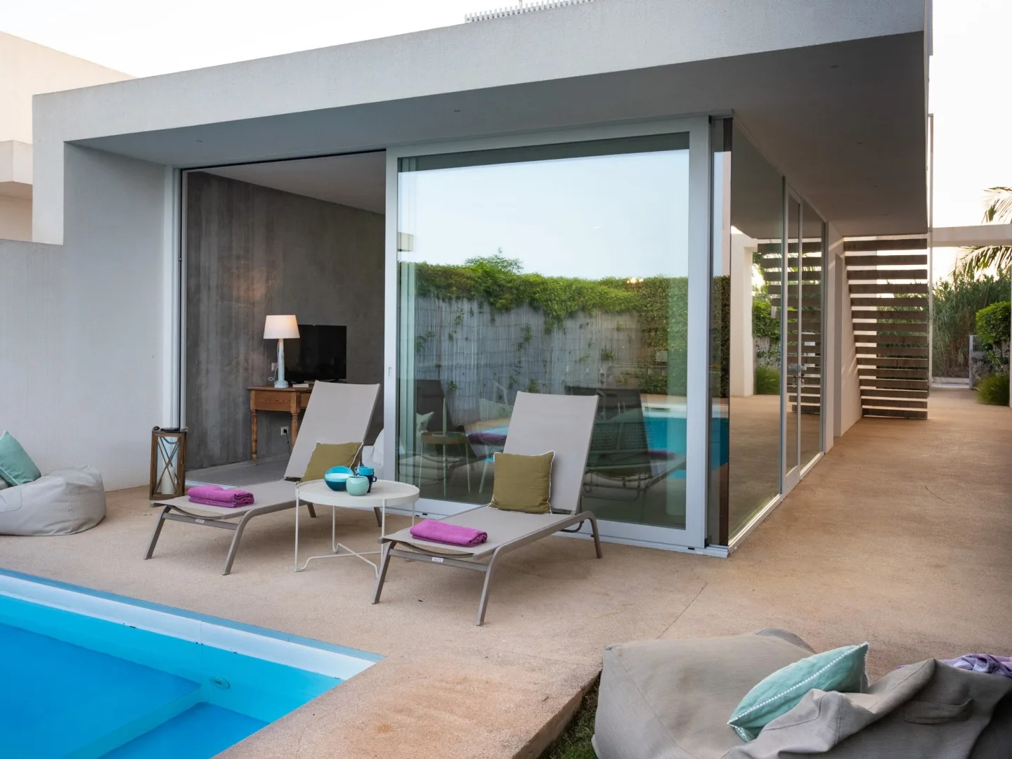 Un patio moderno junto a la piscina, con asientos al aire libre y grandes puertas de vidrio.