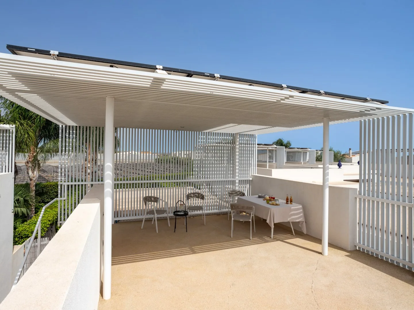 Una zona exterior de comedor queda bajo una pérgola blanca de listones.