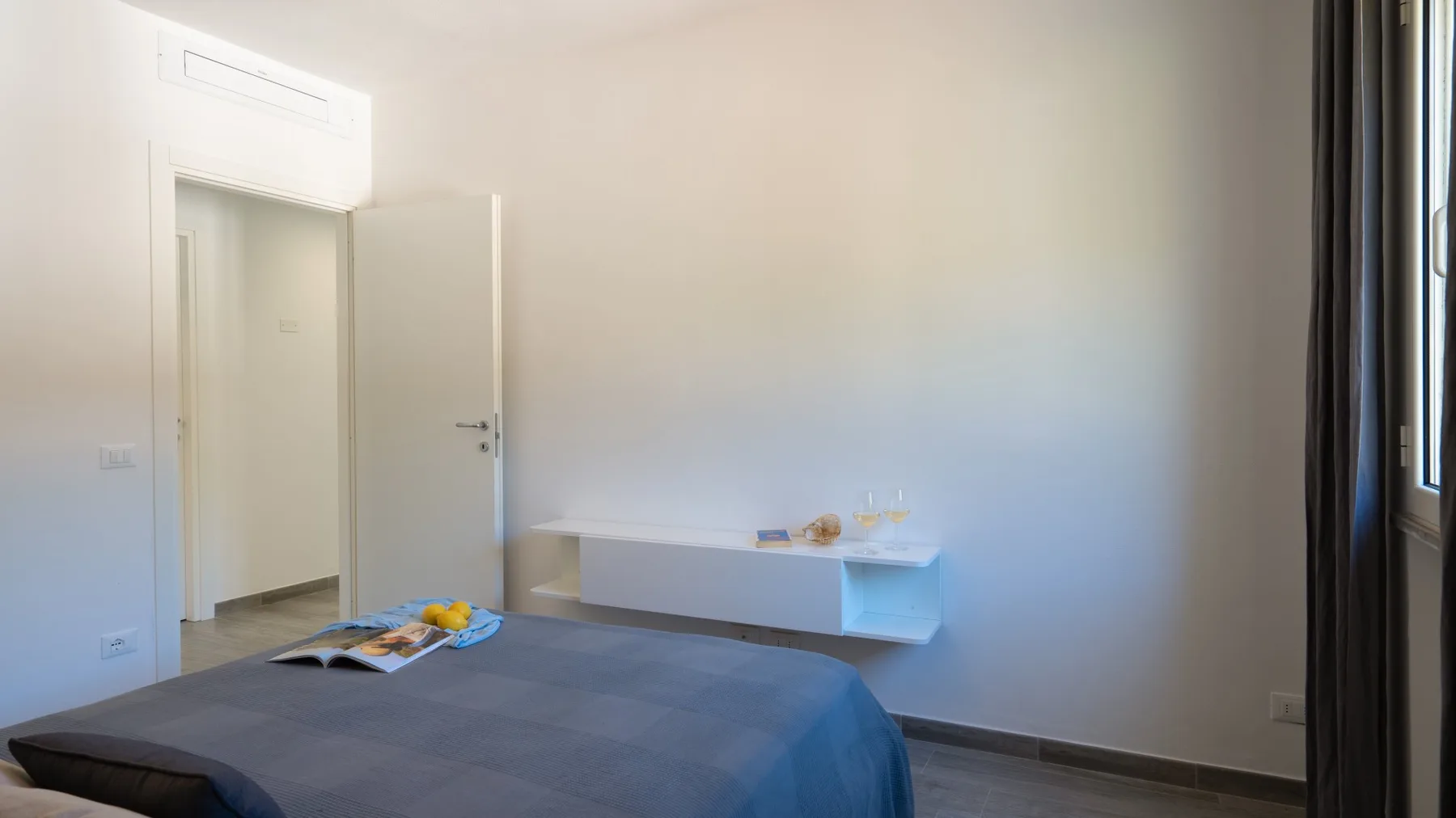 Un dormitorio con una cama, un estante flotante y una ventana.