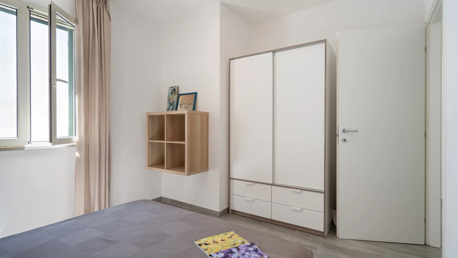 Un dormitorio luminoso con armario empotrado, un pequeño estante de pared y una ventana.