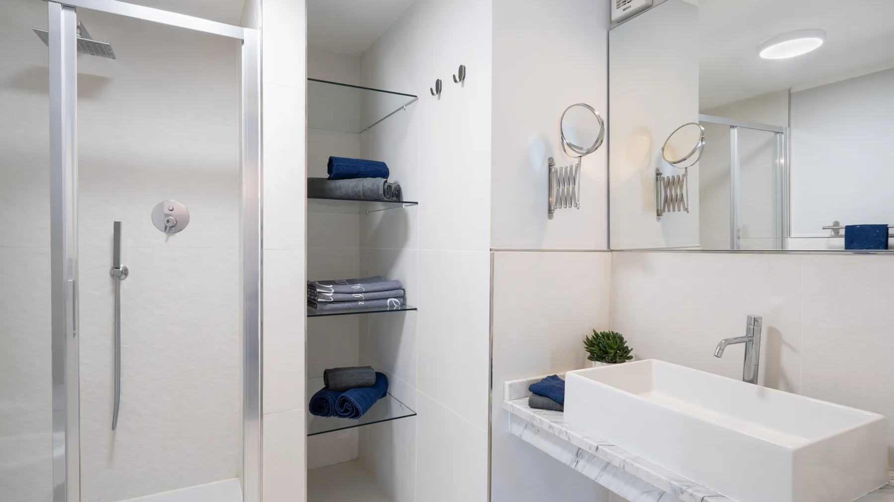 Un baño luminoso con ducha de vidrio, lavabo y estantes abiertos.