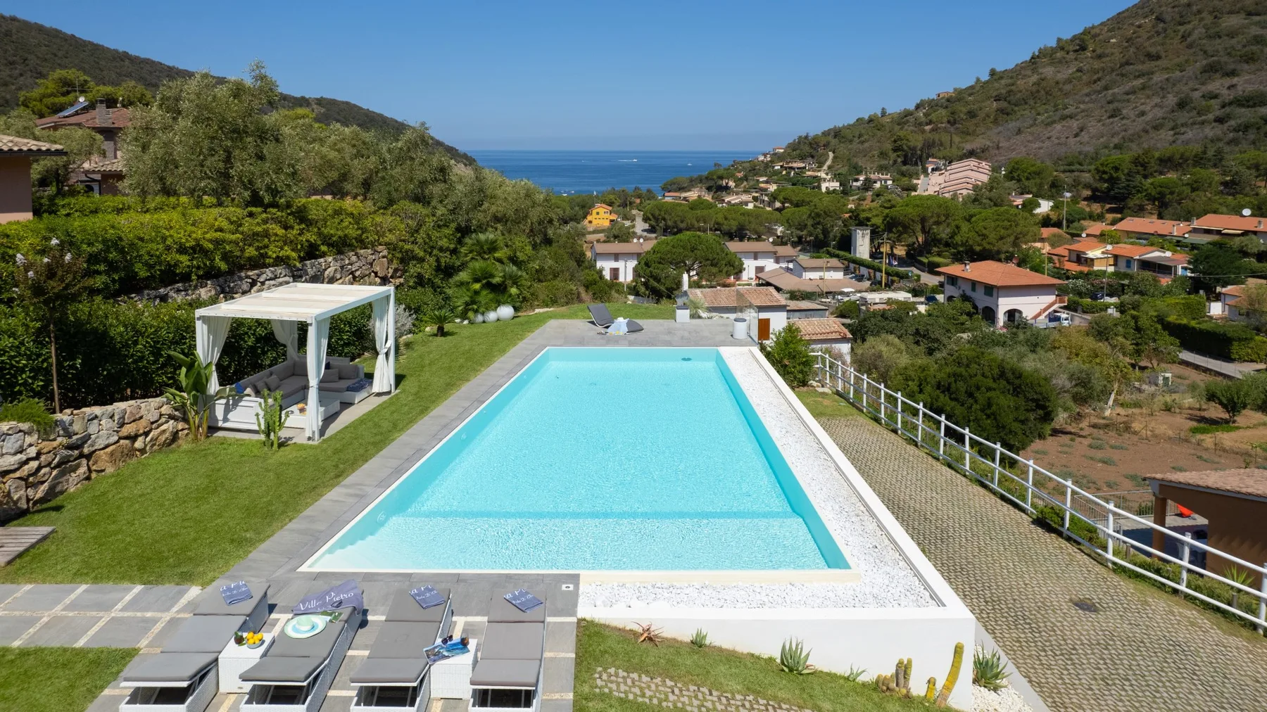 Una piscina ofrece vistas a un vecindario entre colinas verdes y al mar.