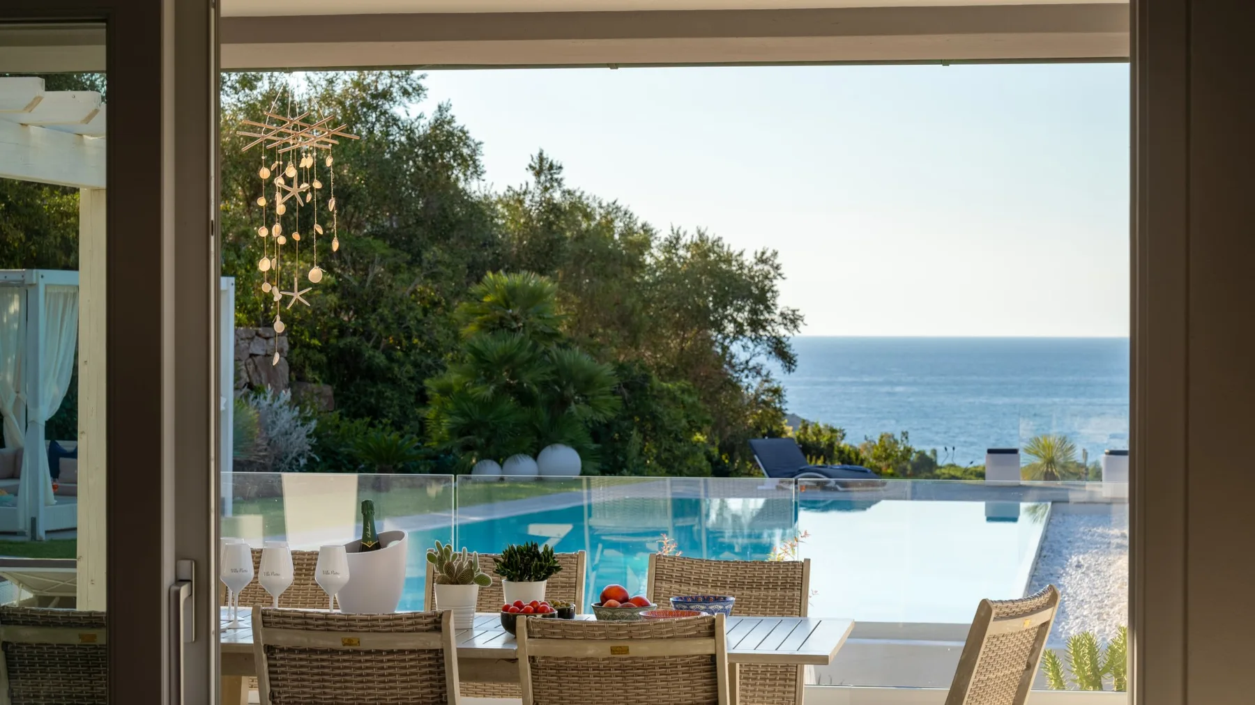 Una terraza junto a la piscina mira al océano, con asientos al aire libre y vegetación.