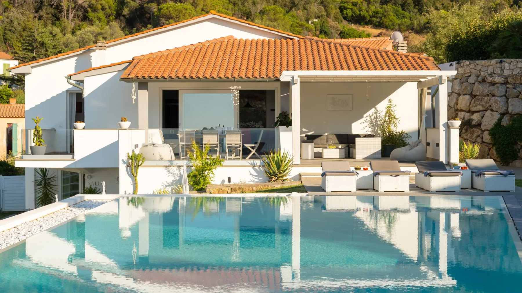 Una casa blanca moderna se abre a una piscina, con asientos junto al agua.