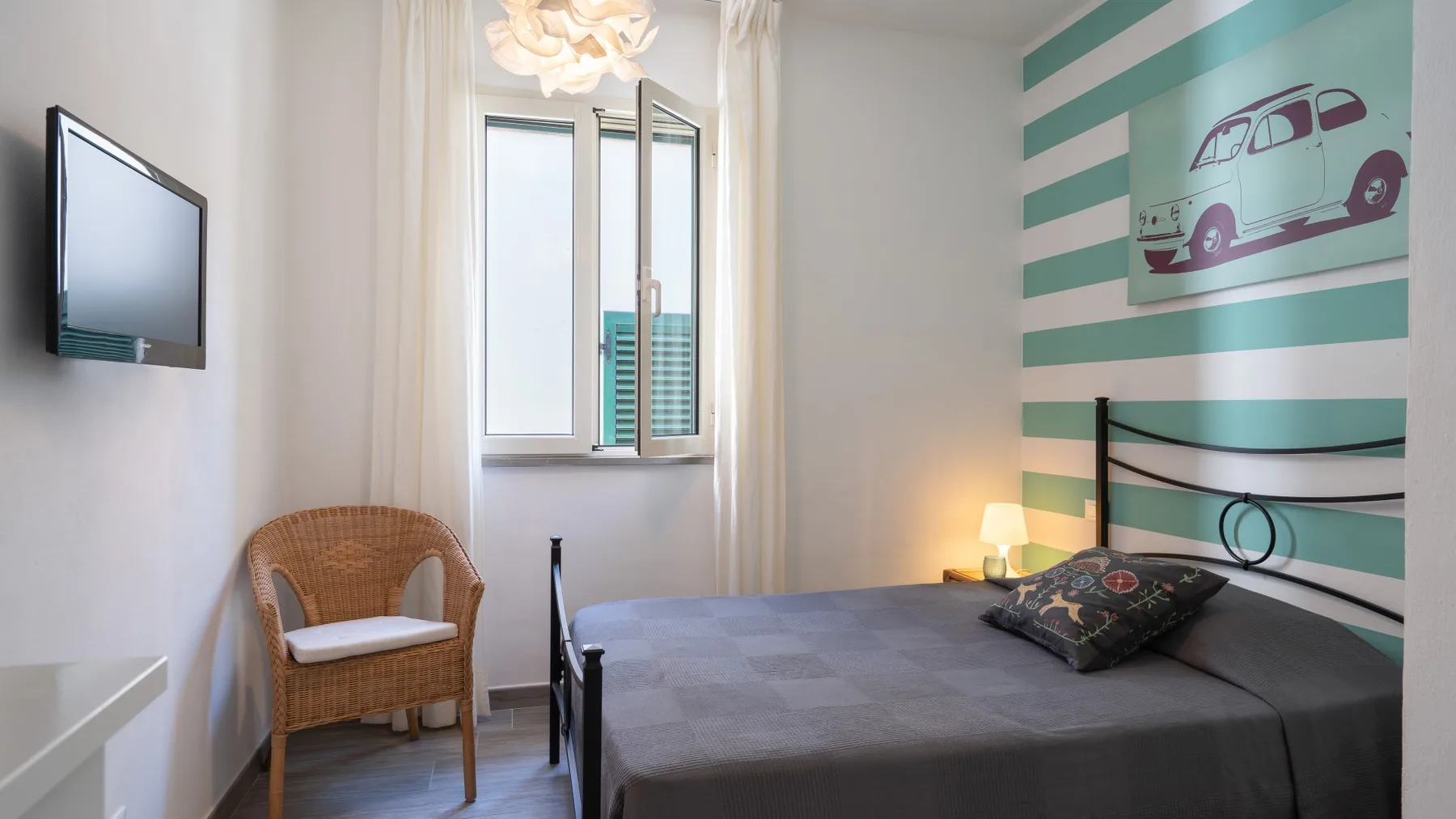 Un dormitorio con una cama, un asiento de mimbre y una ventana.