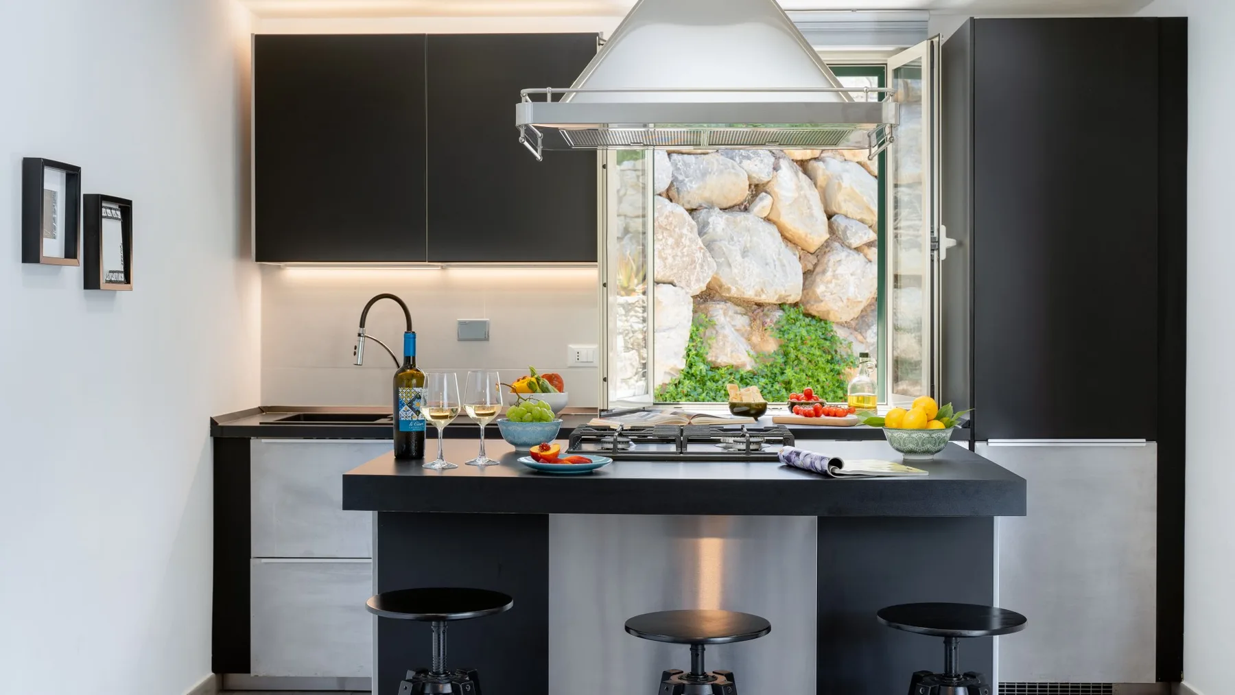 Una cocina moderna con una isla central y una ventana con vista a un jardín rocoso.