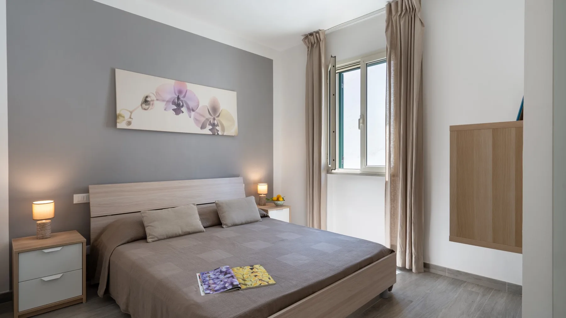 Un dormitorio con una cama junto a una pared gris y una ventana con cortinas.