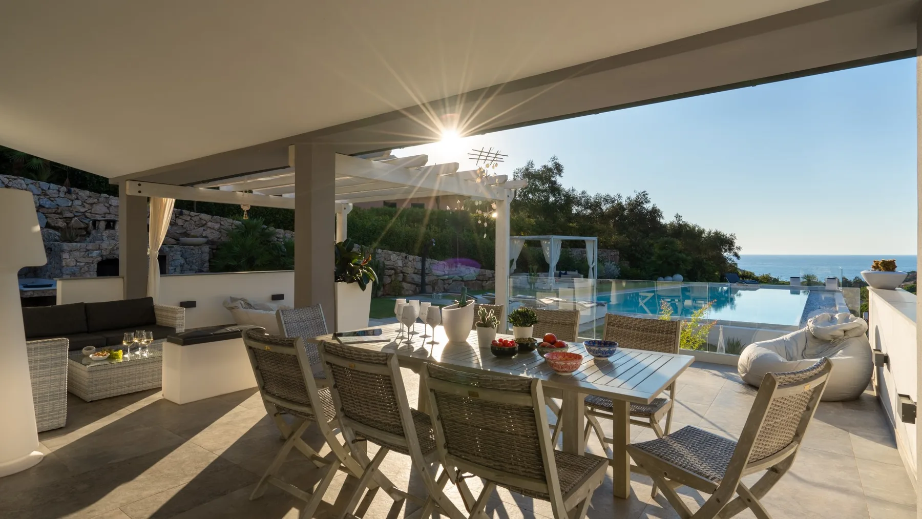 Comedor exterior cubierto con asientos y vistas a una piscina y al mar.