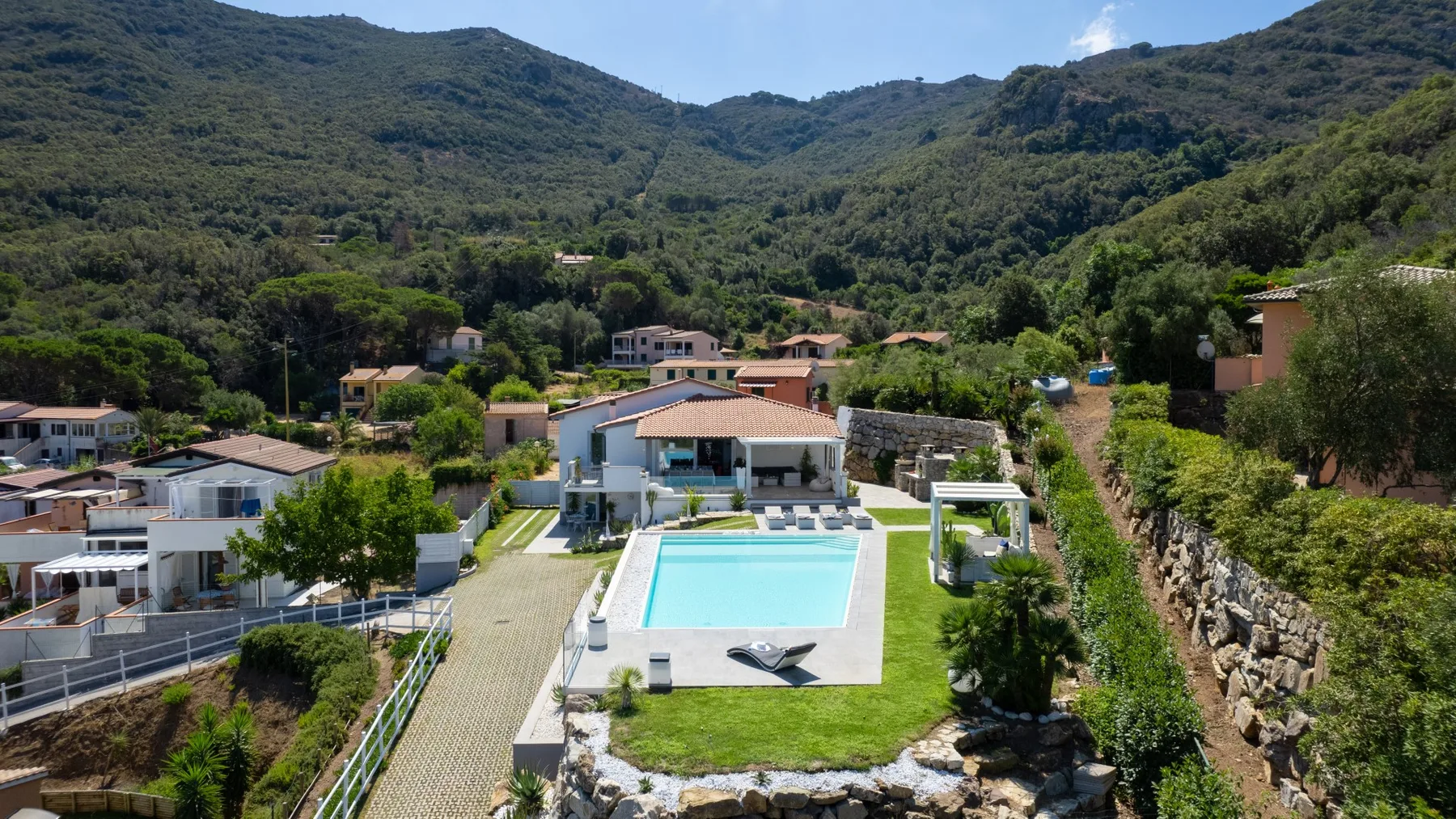 Una zona residencial en la ladera se encuentra entre montañas verdes, con una piscina en primer plano.