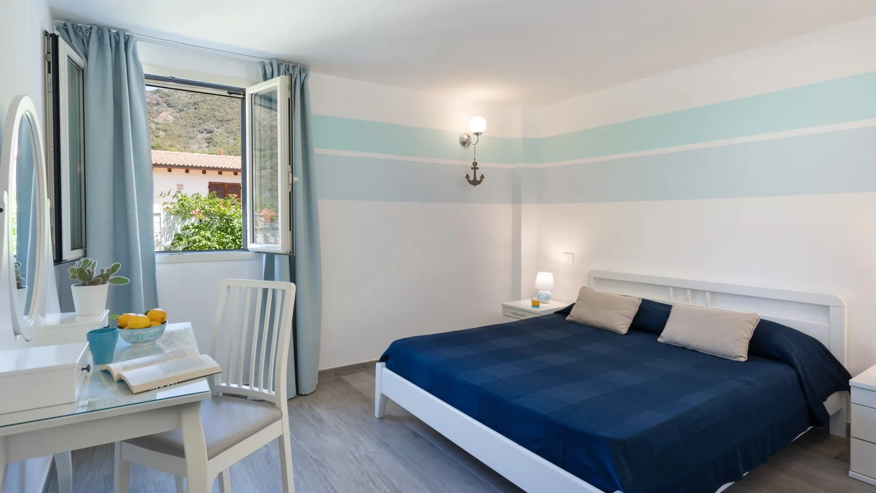 Un dormitorio con una cama azul, un escritorio y una ventana abierta.