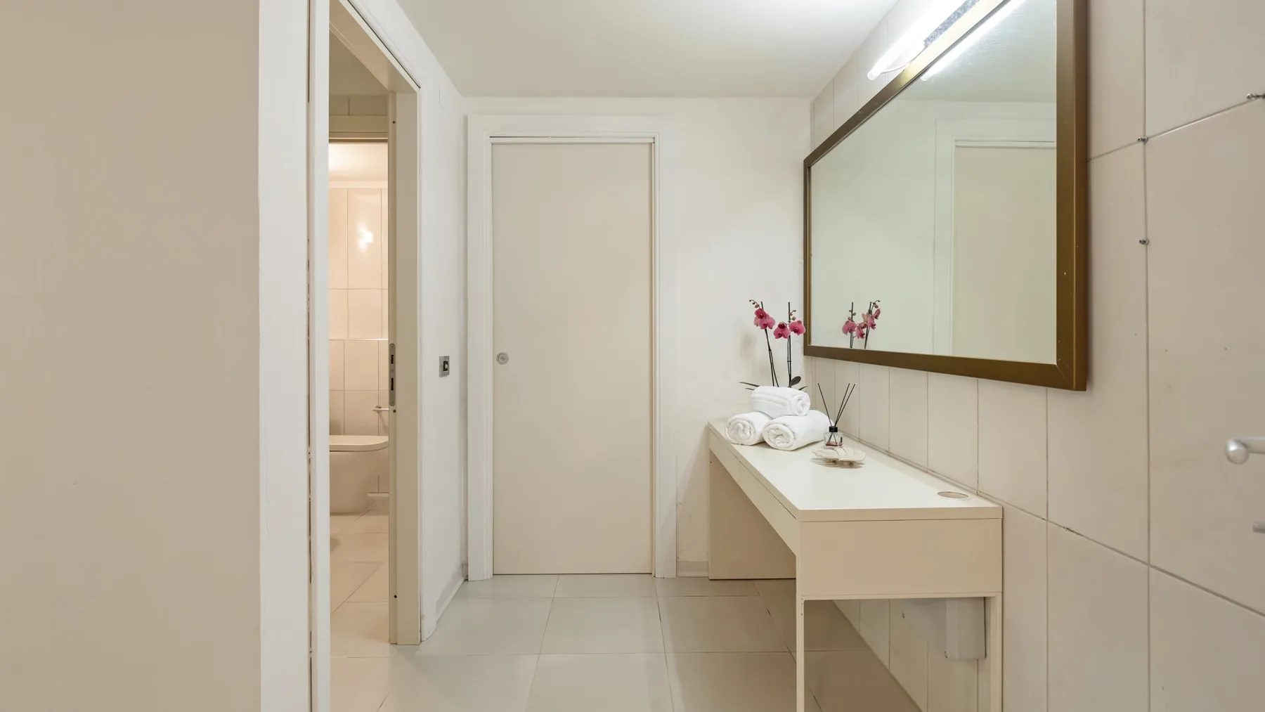 A bright bathroom with a vanity, mirror, and an open doorway to a shower.
