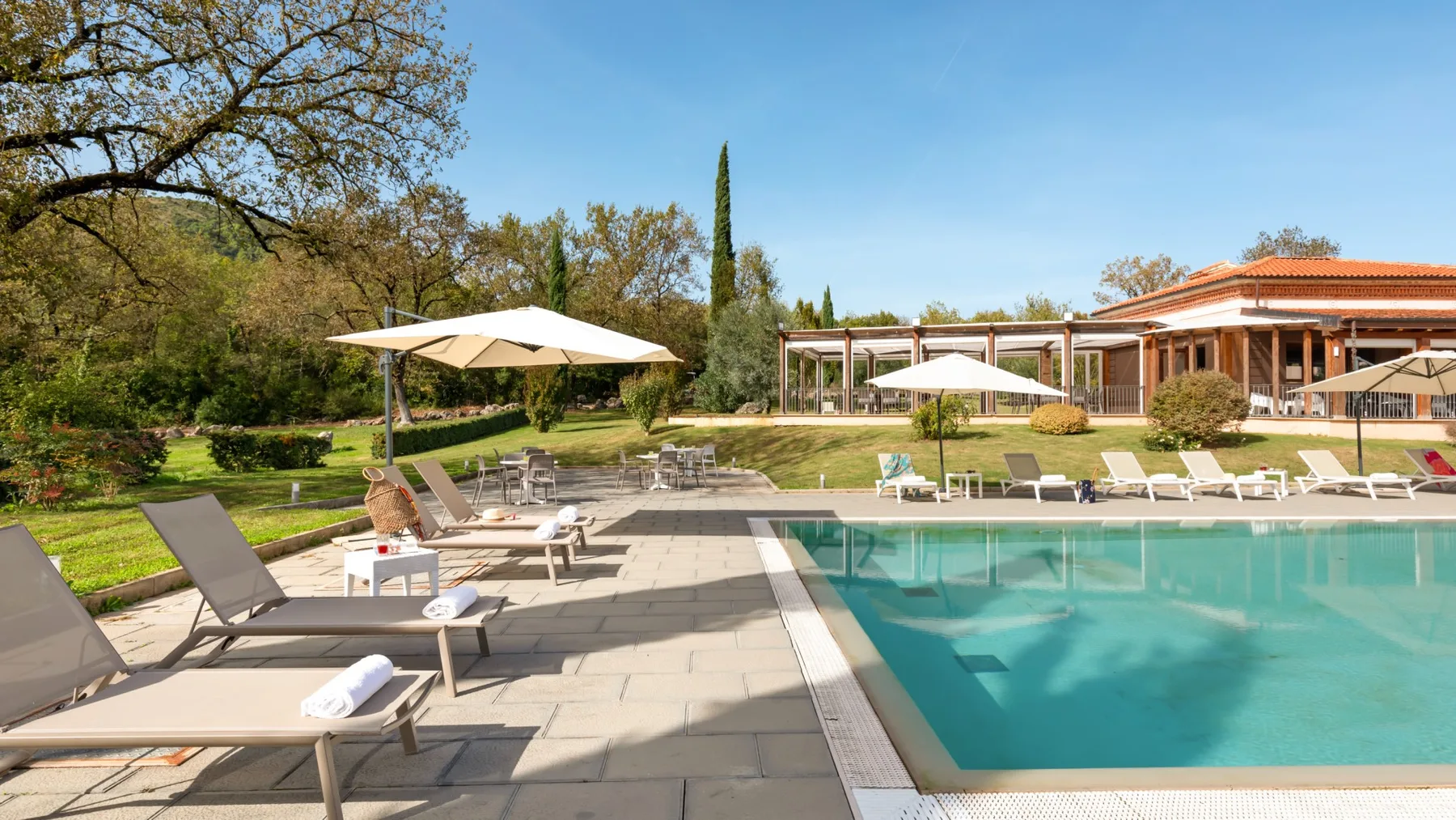 Outdoor swimming pool beside a paved patio with lounge seating and umbrellas.