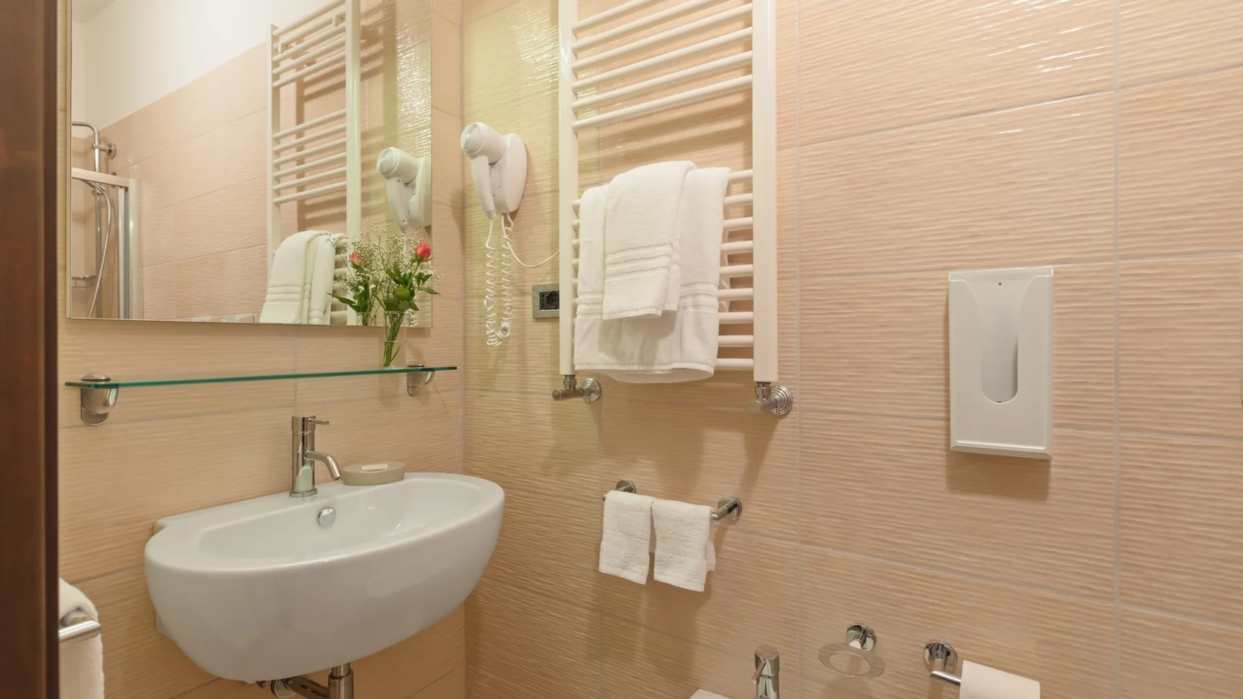 A tiled bathroom with a wall-mounted sink and towels on heated rails.