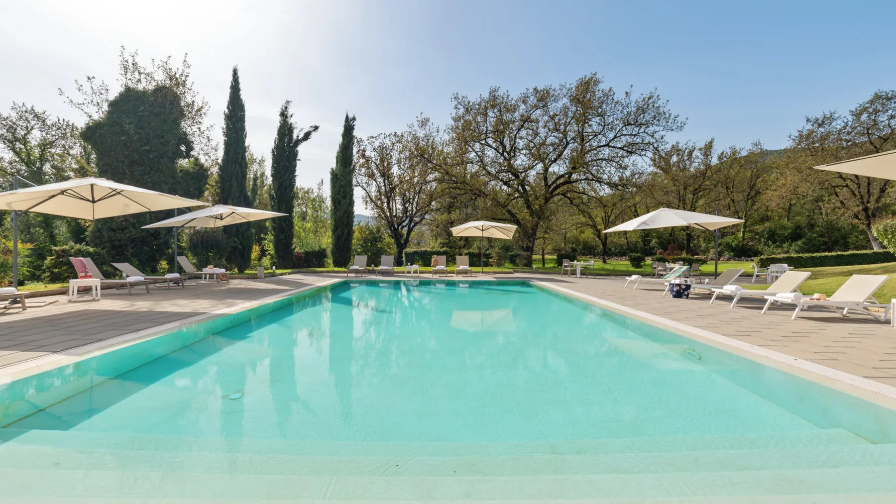 An outdoor swimming pool is surrounded by a deck, lounge seating, and umbrellas.