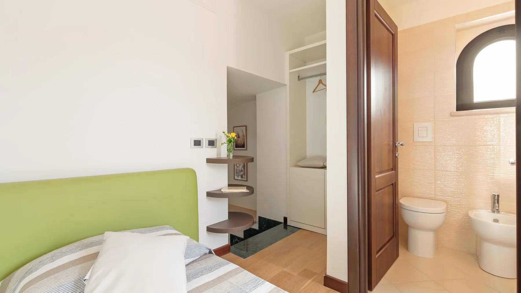 A bedroom with a green headboard sits beside an open doorway to a bathroom.