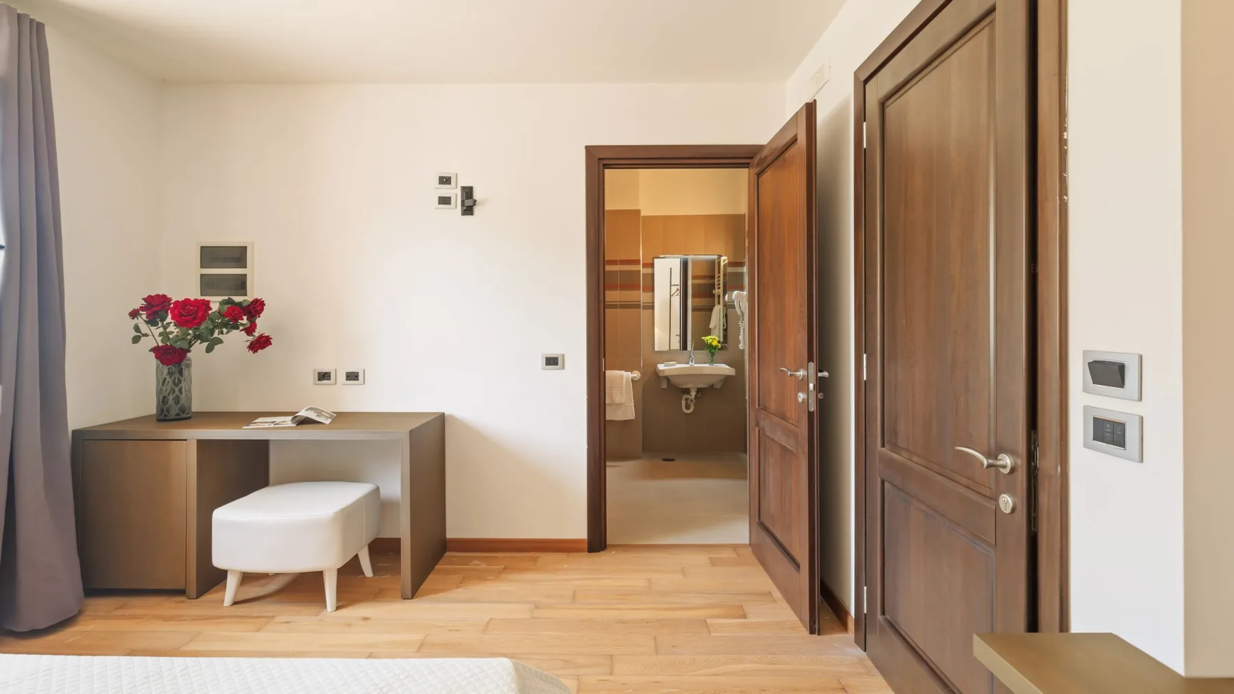 A bright room with a desk, seating, and an open doorway to a sink.